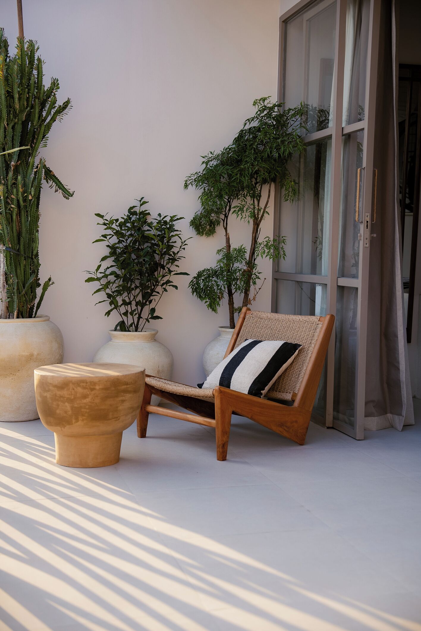 A sunlit outdoor seating area with a wicker lounge chair and a large pot.