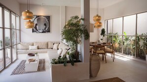 A spacious living area with a large window, a sofa, a coffee table, and a dining table with chairs. - A.K.A House Of Yin & Yang Canggu (Canggu)