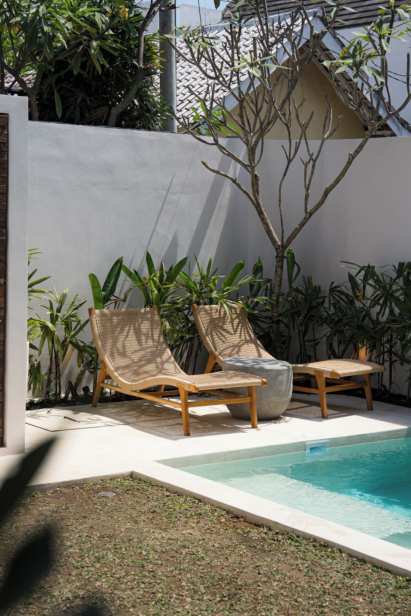 A poolside area with two wicker lounge chairs and a concrete pool.