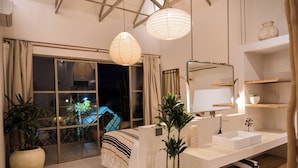 A modern bedroom with a large window, a bedside plant, a white sink, and a wooden shelf. - A.K.A House Of Yin & Yang Canggu (Canggu)