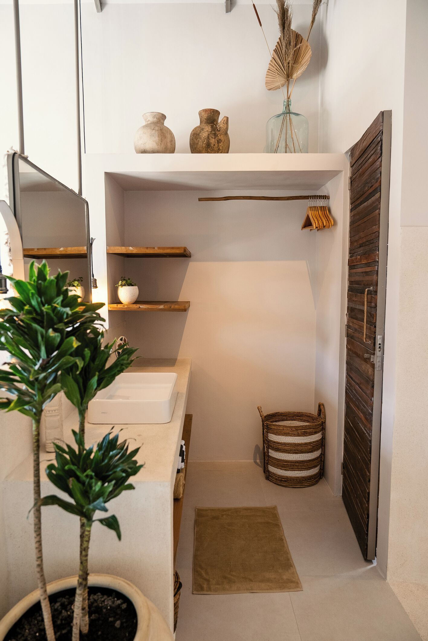 Une petite salle de bain avec un lavabo blanc, une petite plante en pot, un panier en osier et une porte en bois.