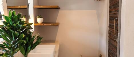Une petite salle de bain avec un lavabo blanc, une petite plante en pot, un panier en osier et une porte en bois.