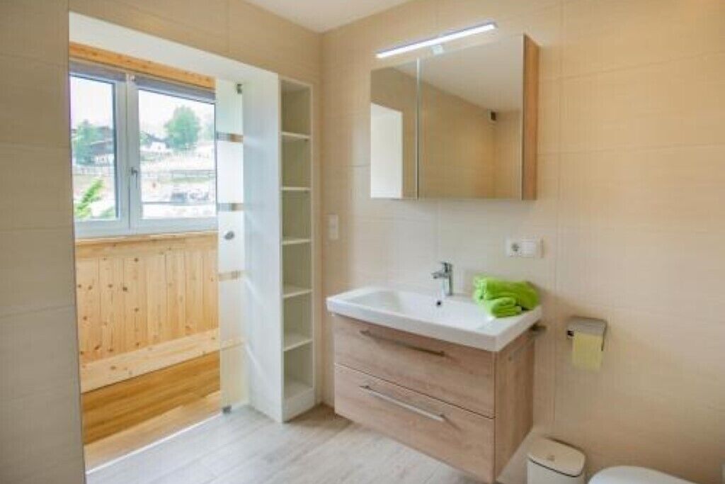 A modern bathroom with a wooden vanity, a large mirror, and a window providing natural light.