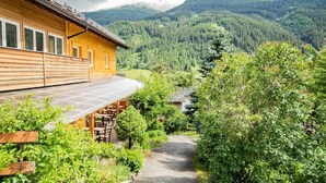 A wooden cabin with a covered outdoor seating area, surrounded by lush greenery and a mountainous backdrop. - Apartment Cafe Max 2 with balcony 55 m2 (Trins)