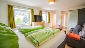 A modern hotel room with two beds, a TV, a sofa, and a large window with curtains. - Apartment Cafe Max 2 with balcony 55 m2 (Trins)