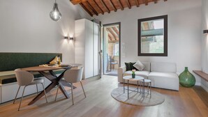 A modern living room with a dining area, wooden flooring, a sofa, a coffee table, and a large window. - Correggiolo Romantic Apartment Pool Montaione Toscana (Montaione)