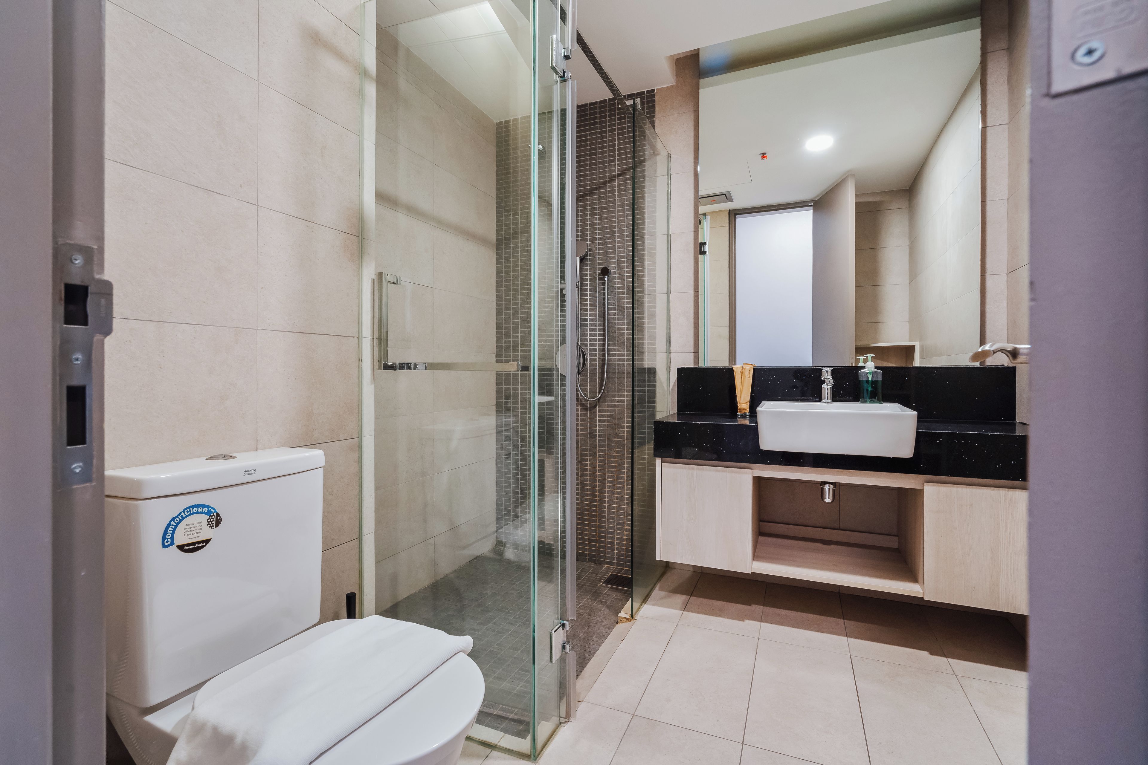 A modern bathroom with a toilet, a glass-enclosed shower, and a sink with a mirror above it.