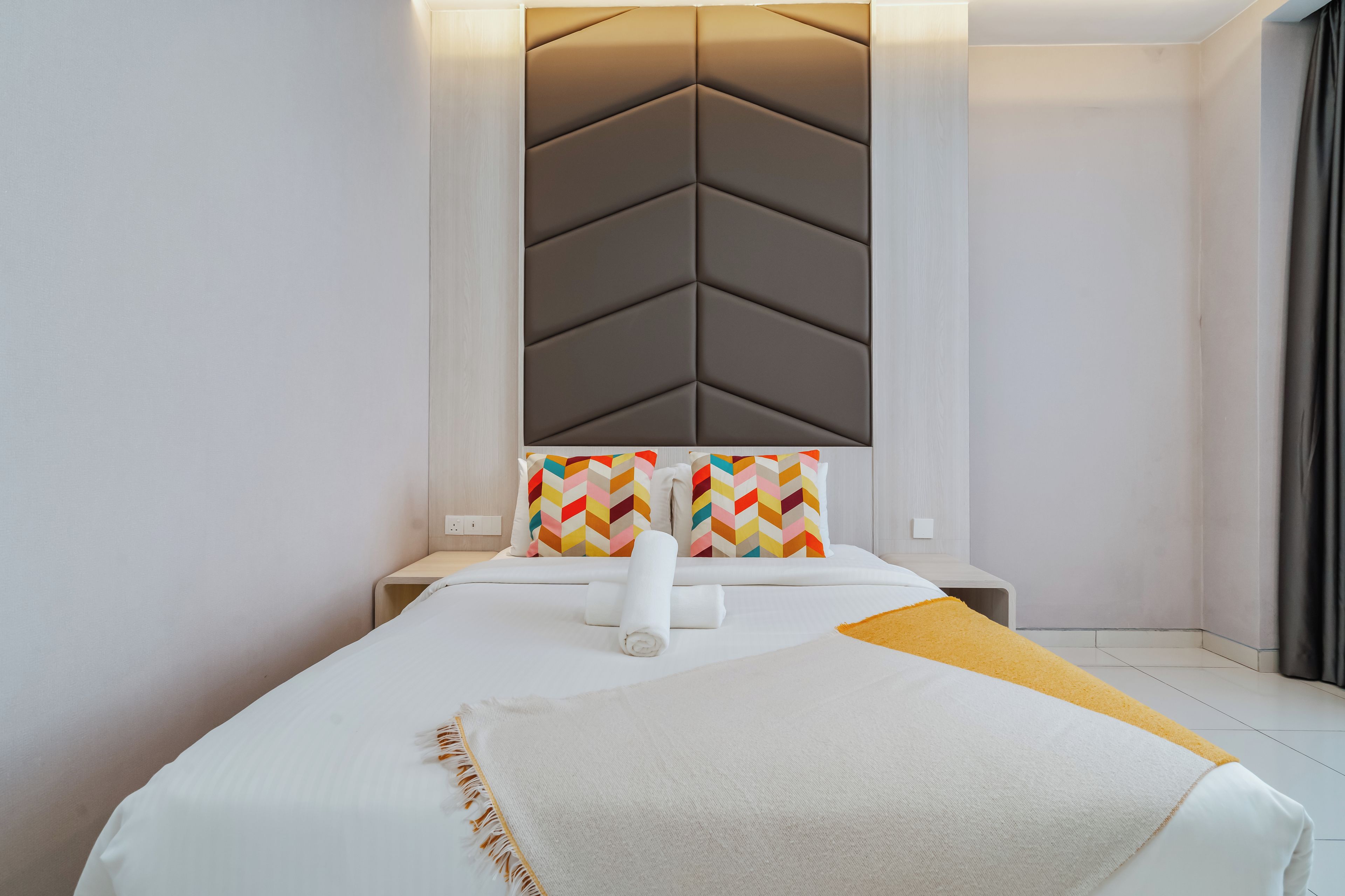 Una habitación de hotel moderna con una cama, un cabecero con diseño geométrico y un cojín colorido.
