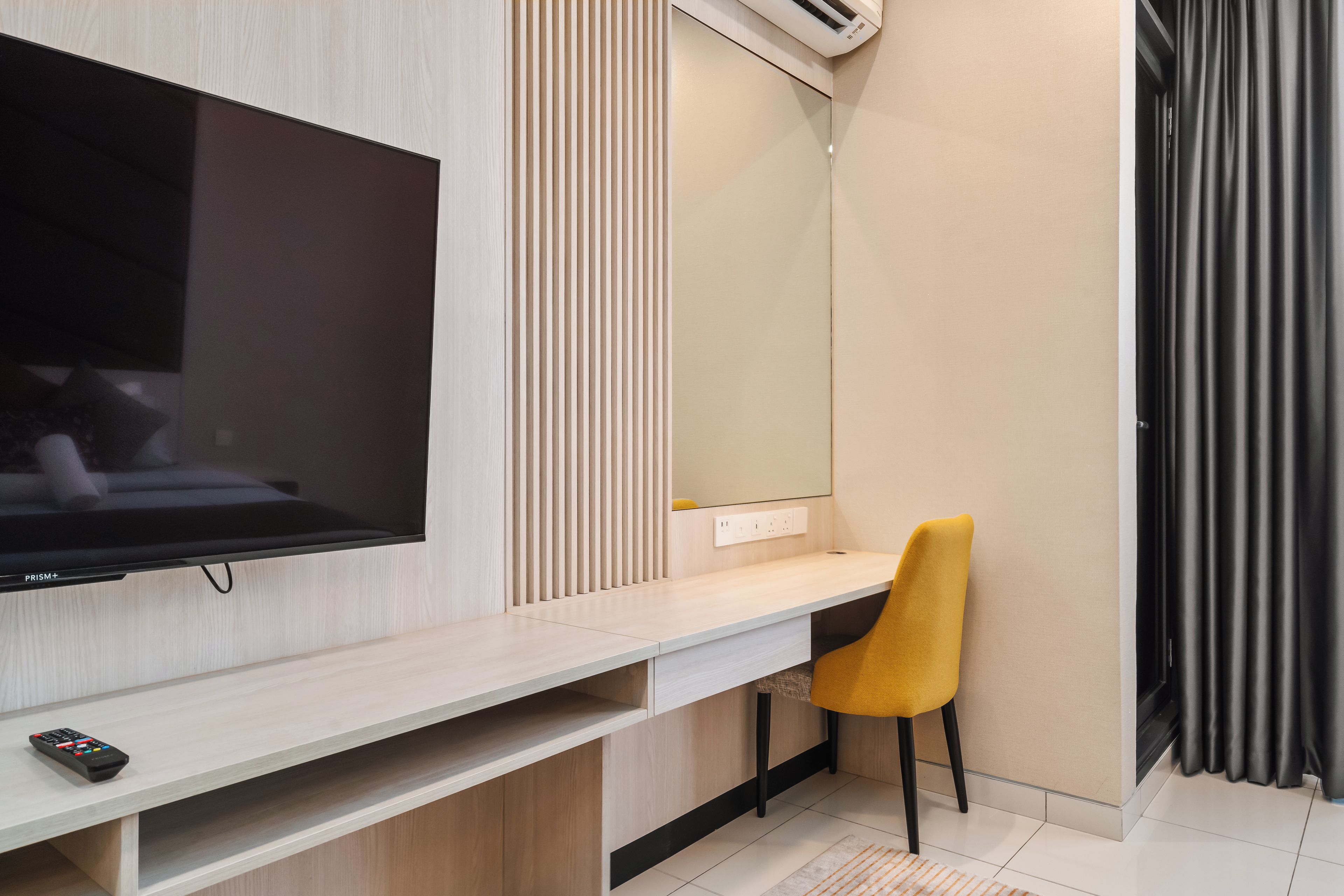 Habitación de hotel moderna con televisor de pantalla plana en la pared, un escritorio de madera con una silla y un espejo grande.