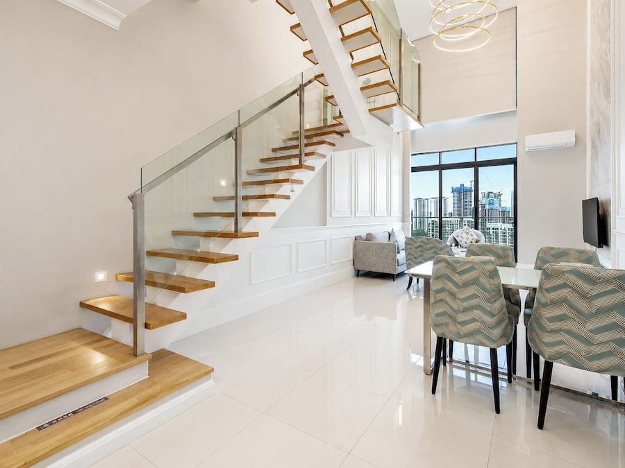 Un interior moderno con una escalera de cristal, un comedor con sillas estampadas y vistas de la ciudad a través de grandes ventanales.