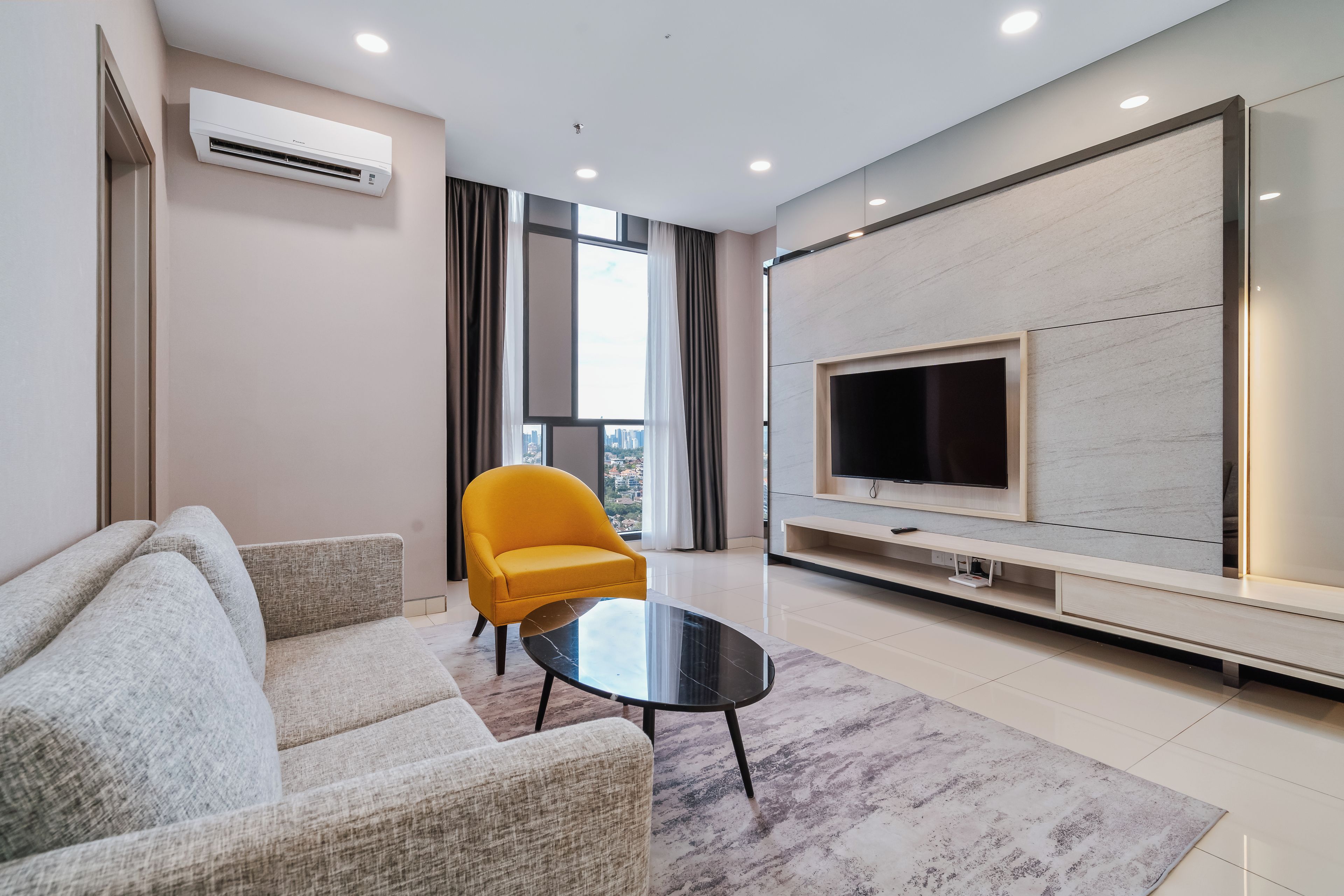 Un salon moderne avec un canapé, un fauteuil jaune, une table basse en verre, un téléviseur à écran plat et une grande fenêtre avec des rideaux.