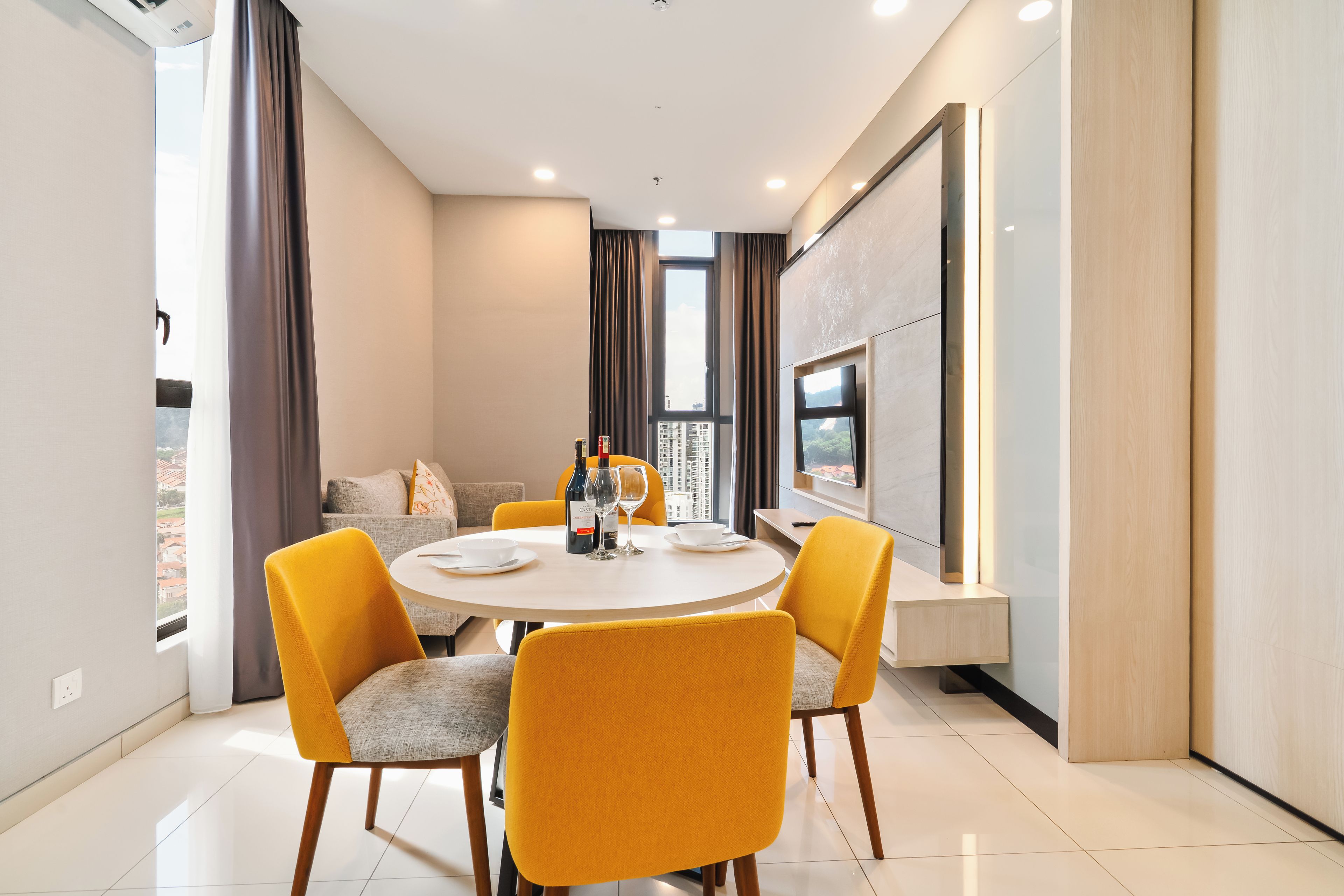 Un espace repas moderne avec une table ronde, quatre chaises jaunes et un canapé en arrière-plan.