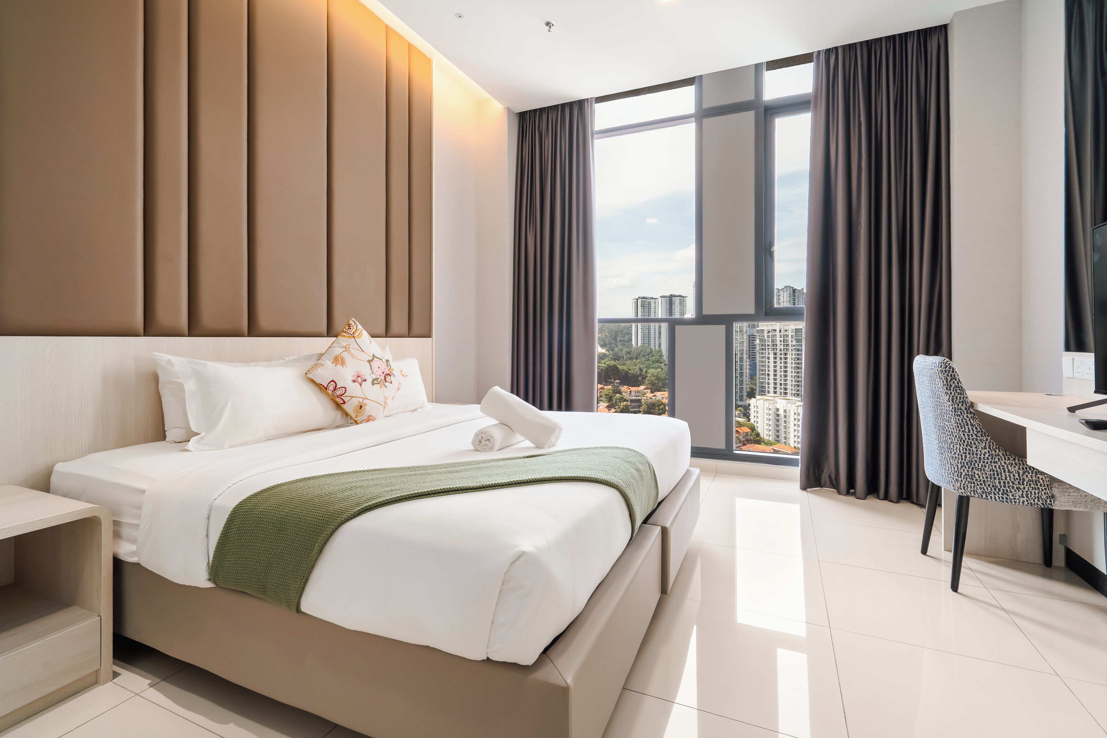 A modern hotel room with a large bed, a desk, and a view of the cityscape.