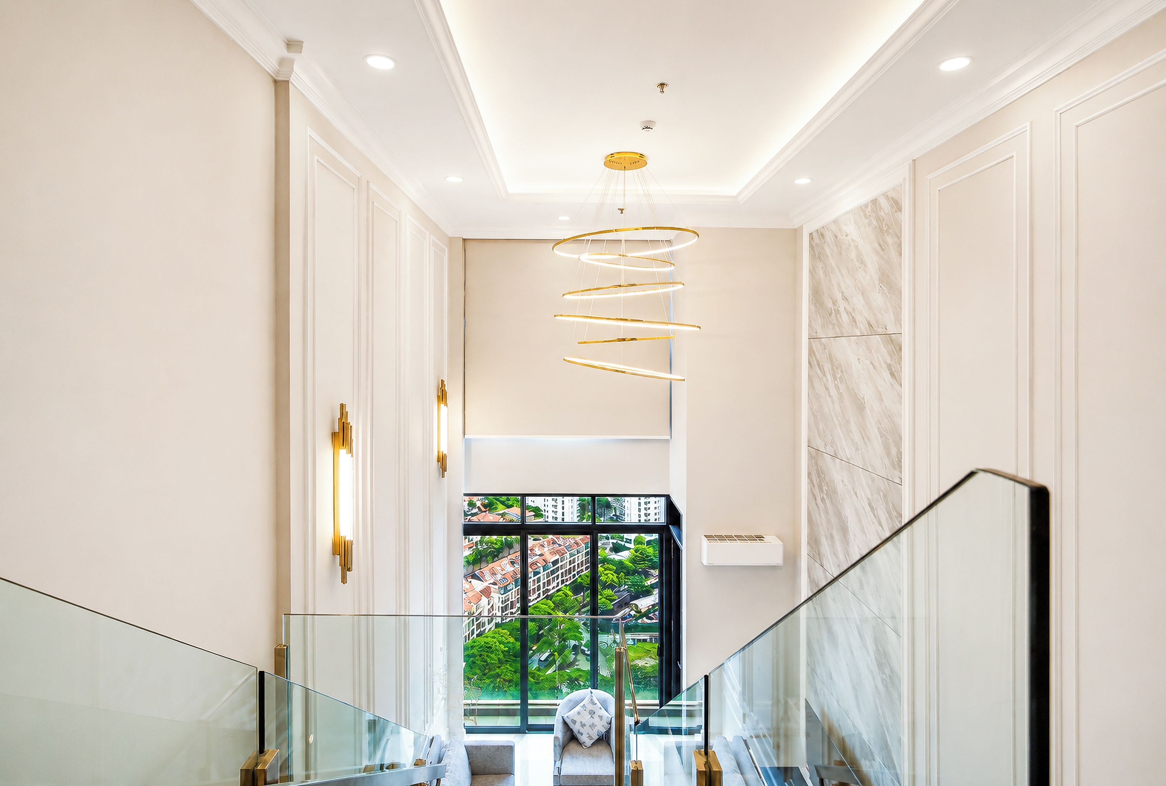 A modern interior with a glass railing staircase, a spiral light fixture, and a view of greenery outside.