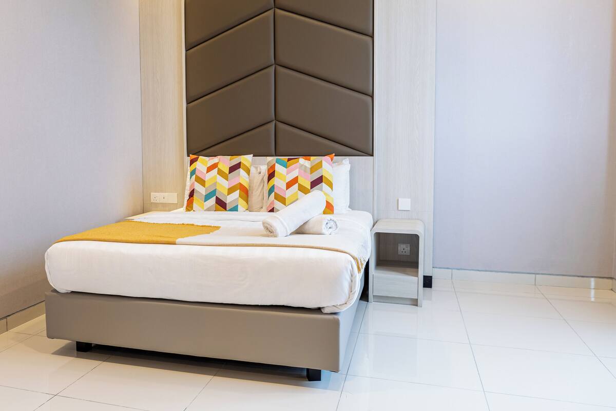 A modern hotel room with a large bed, a headboard with a geometric pattern, and a bedside table with a power outlet.