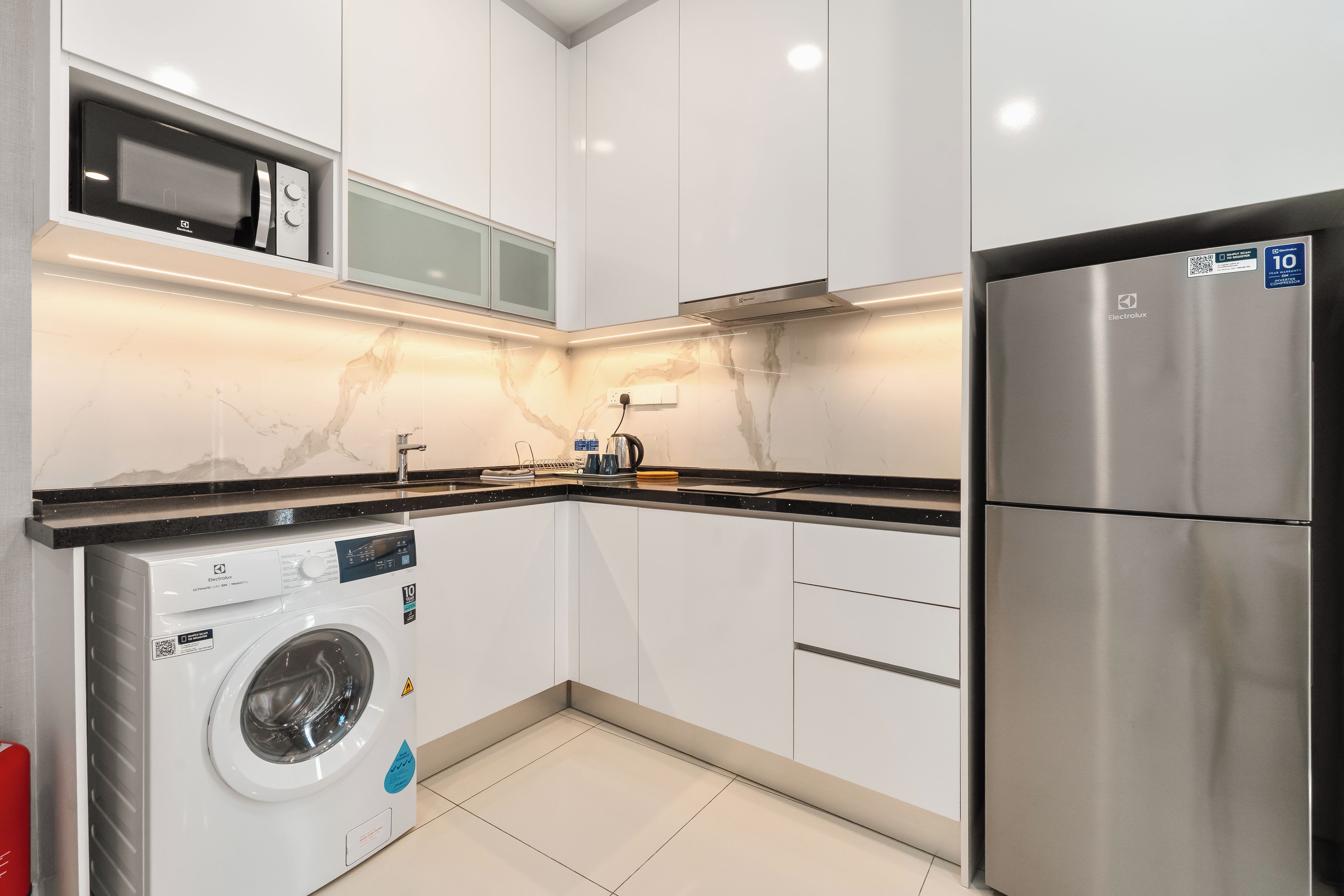A modern kitchen with a built-in washing machine, a stainless steel refrigerator, and a microwave.