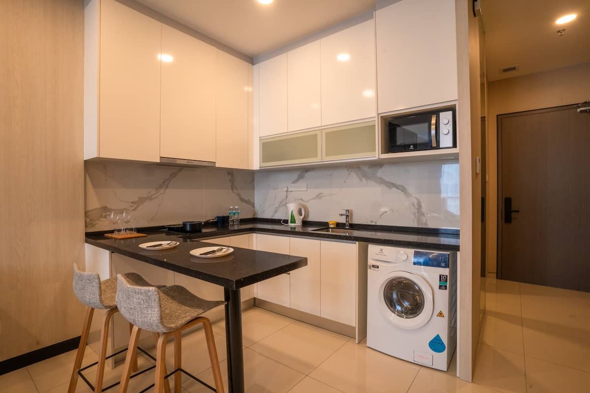 A modern kitchen with white cabinets, a marble backsplash, a built-in washing machine, and a small bar area with stools.