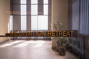 Un espacio interior amplio con un gran ventanal, una planta en maceta y el texto "MEDITATION RETREAT".
