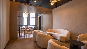 Un área de estar moderna con asientos cómodos, una pequeña mesa y vista hacia un comedor.