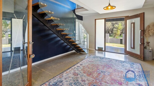 A modern interior with a glass staircase, a patterned rug, and a view of the outdoors.