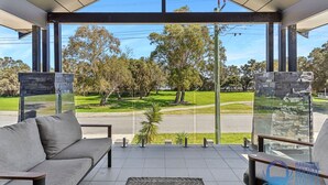 A modern room with a glass wall, a grey sofa, and a view of a park.