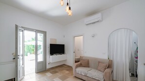 A living room with a beige sofa, a flat-screen TV, a ceiling light fixture, and a door leading outside.