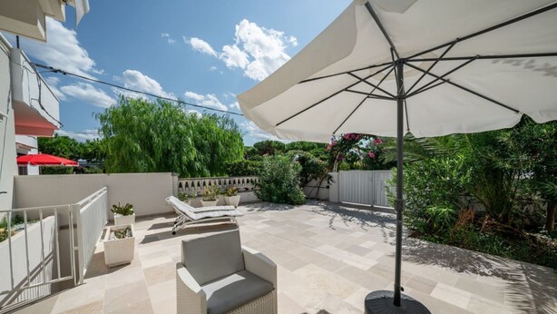 An outdoor patio with a white umbrella, wicker furniture, and potted plants.