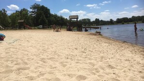 En sandstrand med en trækonstruktion, en legeplads og en rolig sø.