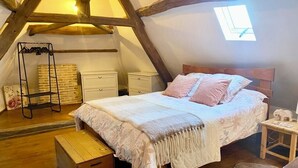 Et hyggeligt soveværelse under skråvæggen med træloft, seng med pink sengetøj, et lille natbord og en rustik træbænk.