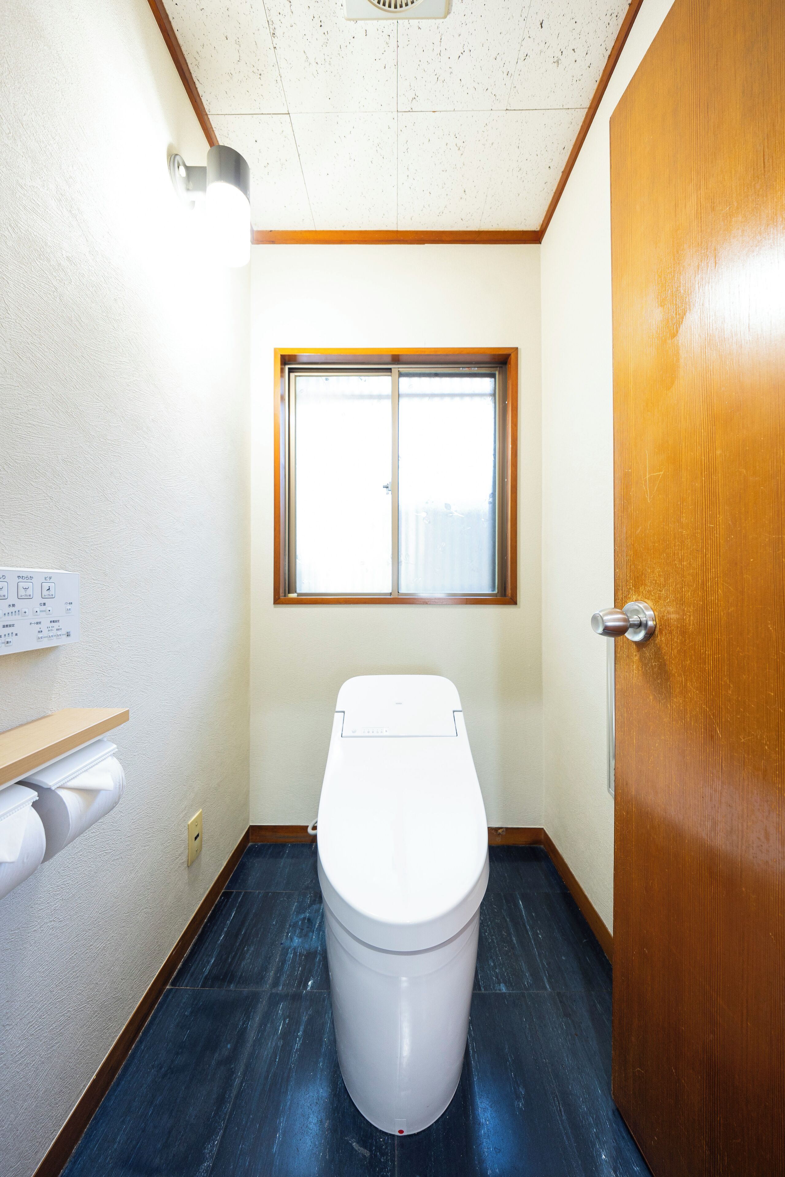 A compact bathroom with a toilet, a window, and a wooden door.