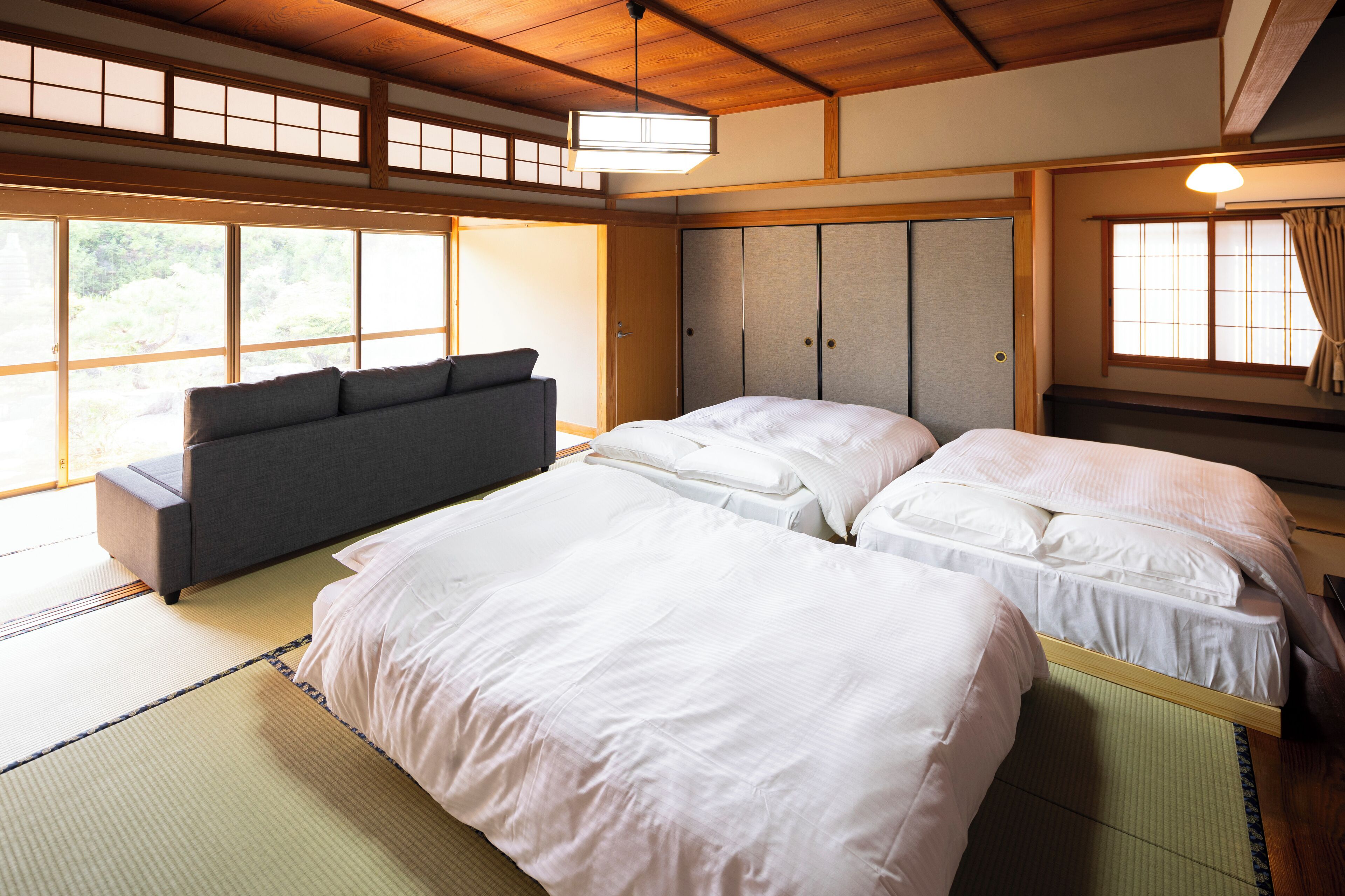 A traditional Japanese-style bedroom with tatami flooring, a futon bed, a low wooden bed frame, and sliding shoji doors.