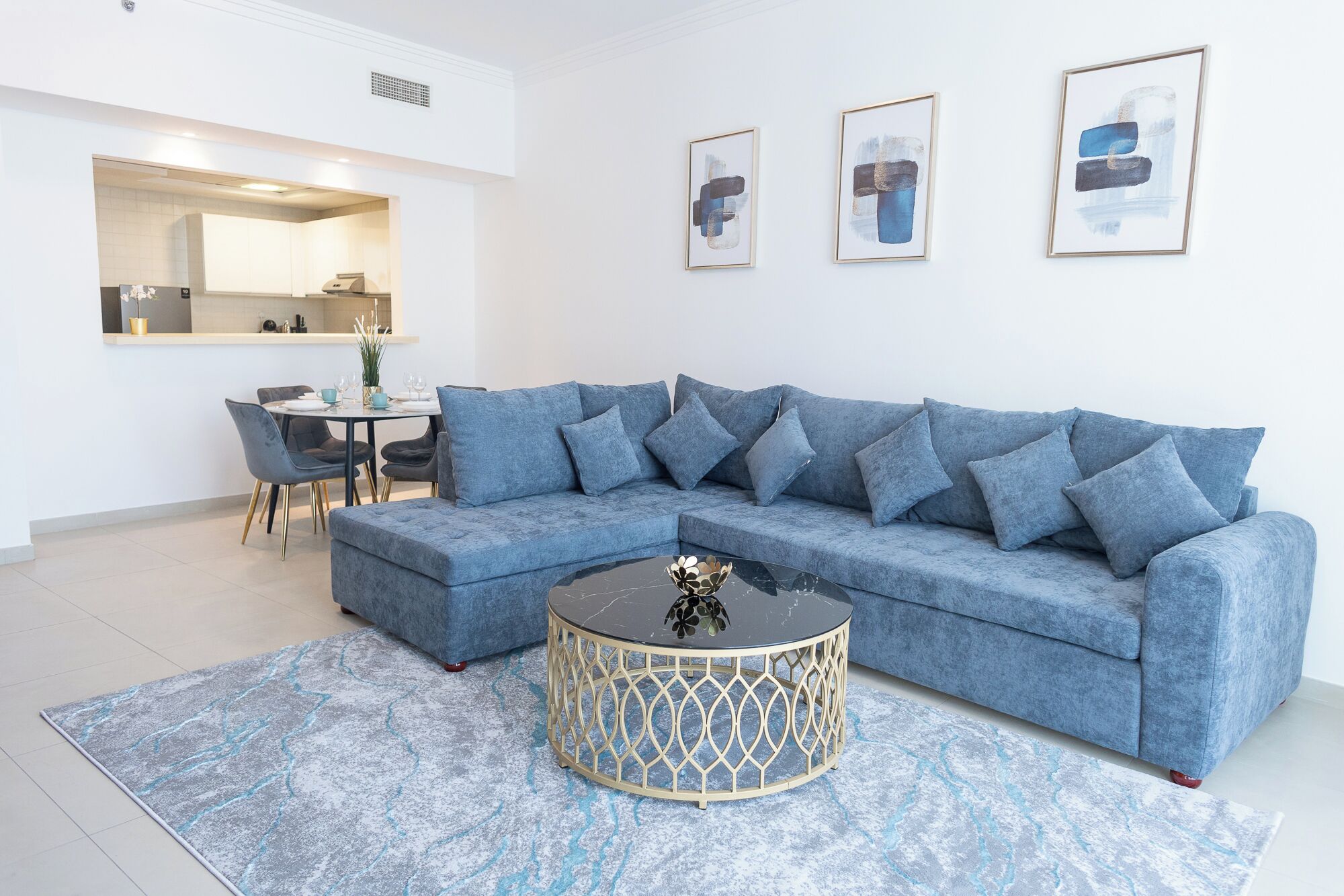 Uma sala de estar moderna com um sofá seccional, uma mesa de centro redonda e um espaço de jantar com uma pequena mesa e cadeiras.