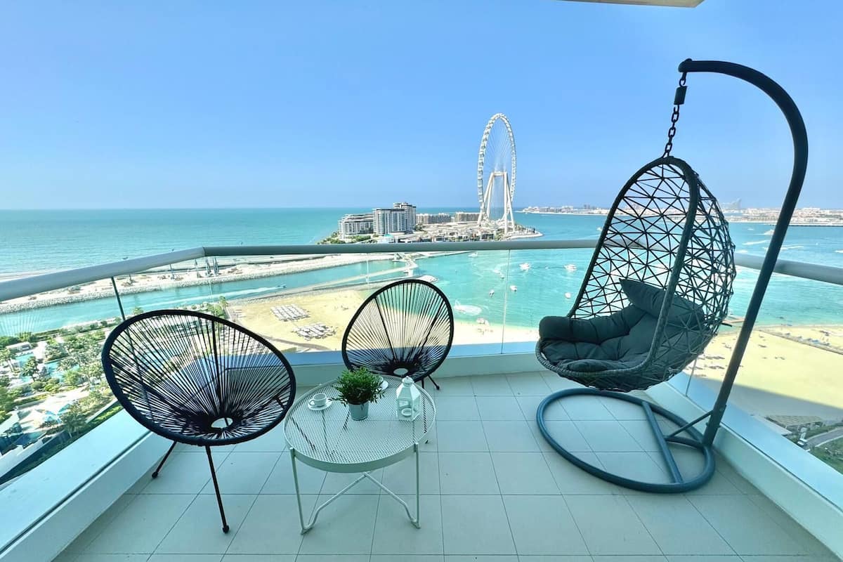 Un balcon avec deux chaises, un fauteuil suspendu et une petite table sur laquelle est posée une plante.