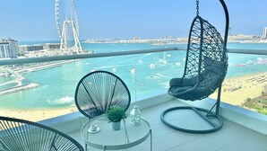 A balcony with a hanging chair, a round table with a potted plant, and a view of a large Ferris wheel and marina. - HAPPY SEASON I Al Bateen Residences  (Dubai)