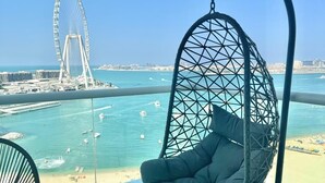 A balcony with a hanging chair, a view of the sea, and a Ferris wheel in the distance. - HAPPY SEASON I Al Bateen Residences  (Dubai)