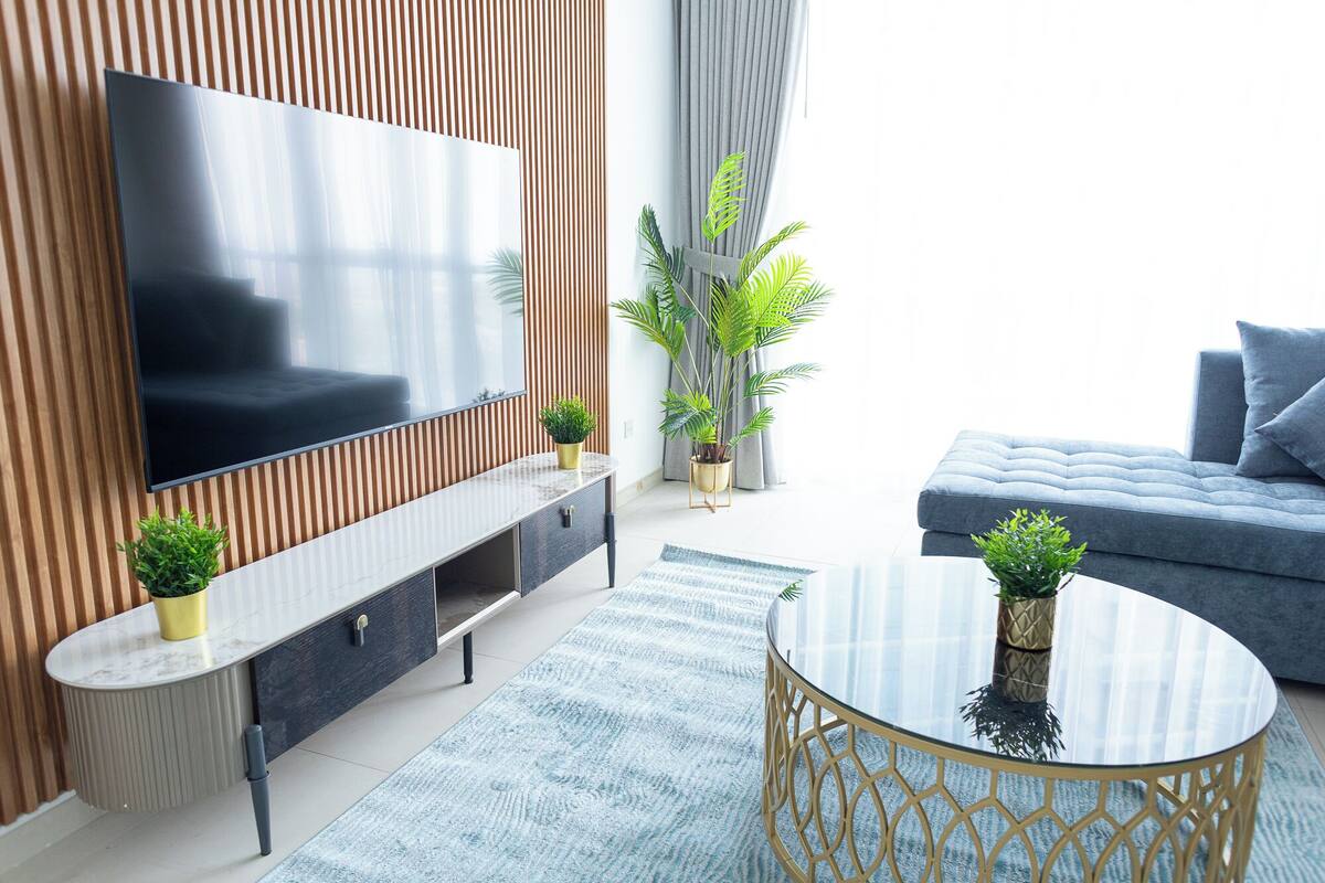 Un salon moderne avec un téléviseur à écran plat, un canapé gris et des plantes décoratives.