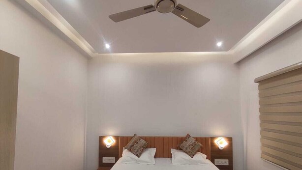 Un dormitorio con cama, ventilador de techo, lámparas de noche y una ventana con persianas.