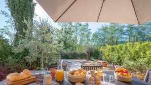 Mesa de comedor al aire libre con alimentos para el desayuno, rodeada de vegetación exuberante y un cielo despejado.