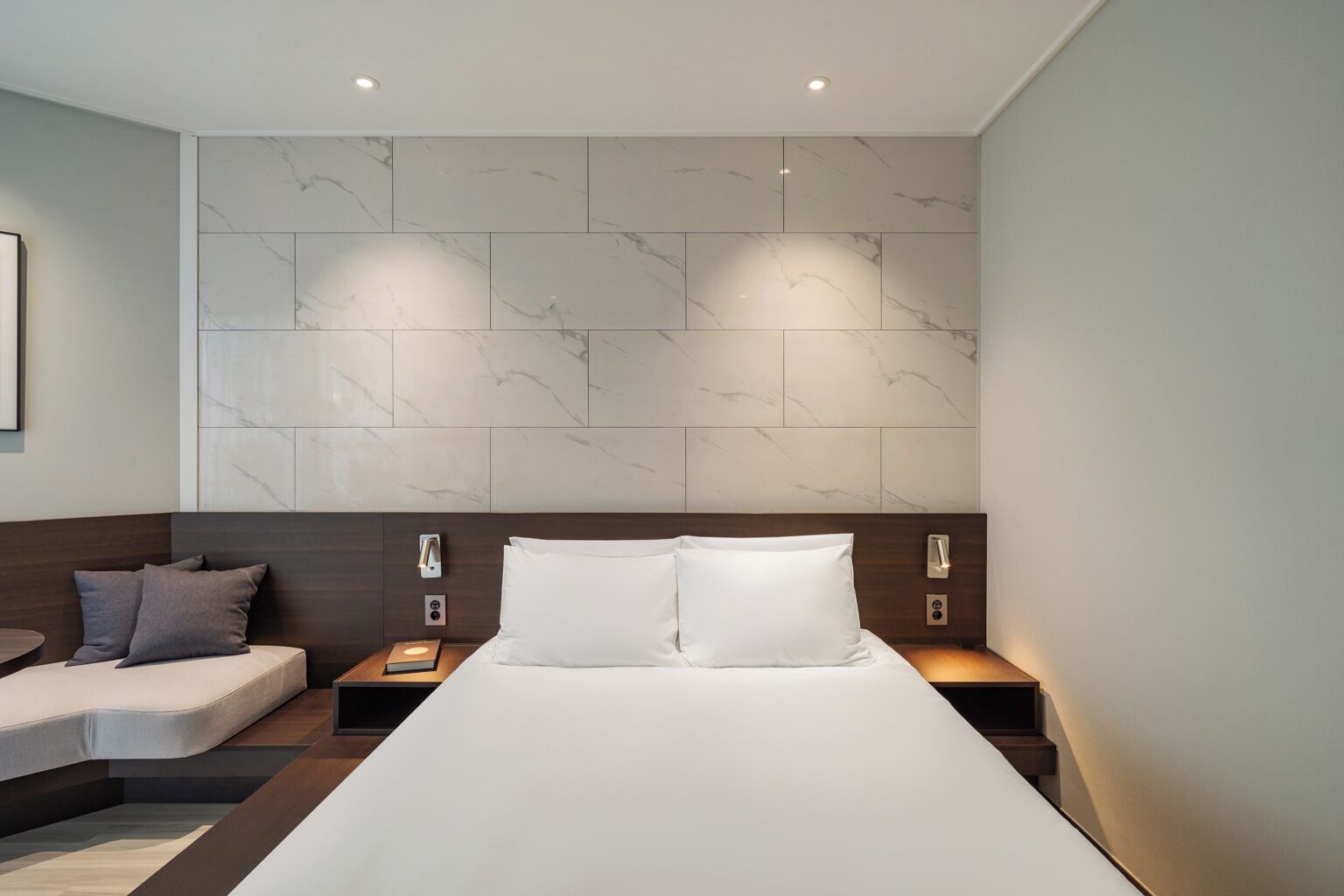 Een moderne hotelkamer met een groot bed, twee nachtkastjes, een slaapbank en wanden met een marmerlook.