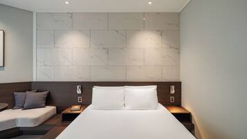 Een moderne hotelkamer met een groot bed, twee nachtkastjes, een slaapbank en wanden met een marmerlook.