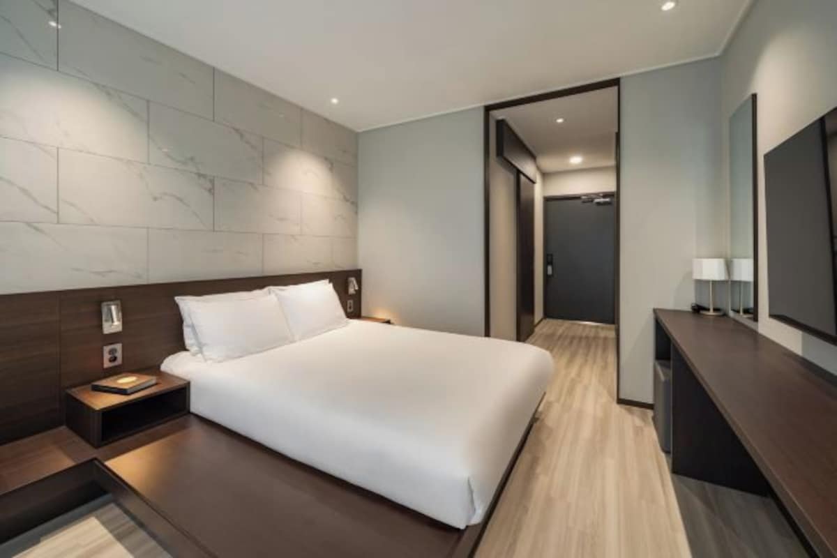 A modern hotel room with a large bed, a bedside table, a nightstand, a desk, and a large mirror.