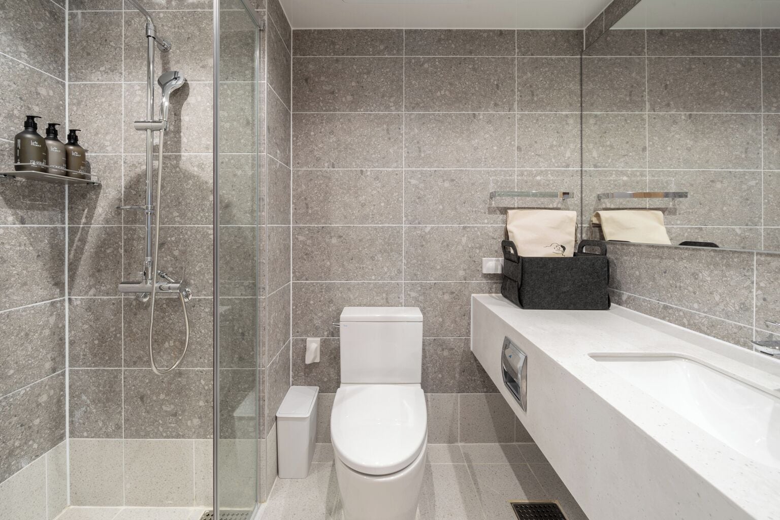 A modern bathroom with a glass-enclosed shower, a white toilet, and a large vanity with a mirror.