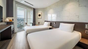 A hotel room with two beds, a desk, a chair, a small table, and a large window with a view.