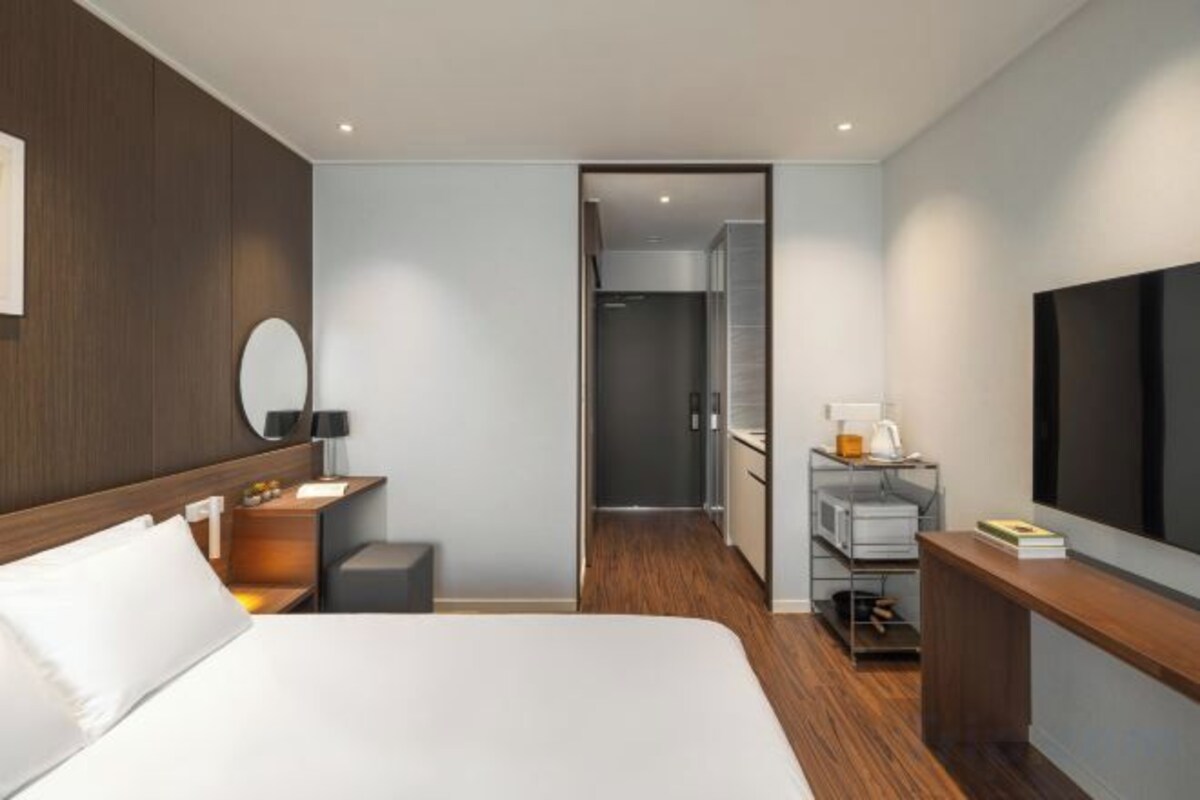 Una habitación de hotel moderna con una cama grande, mesita de noche, espejo y televisor montado en la pared.