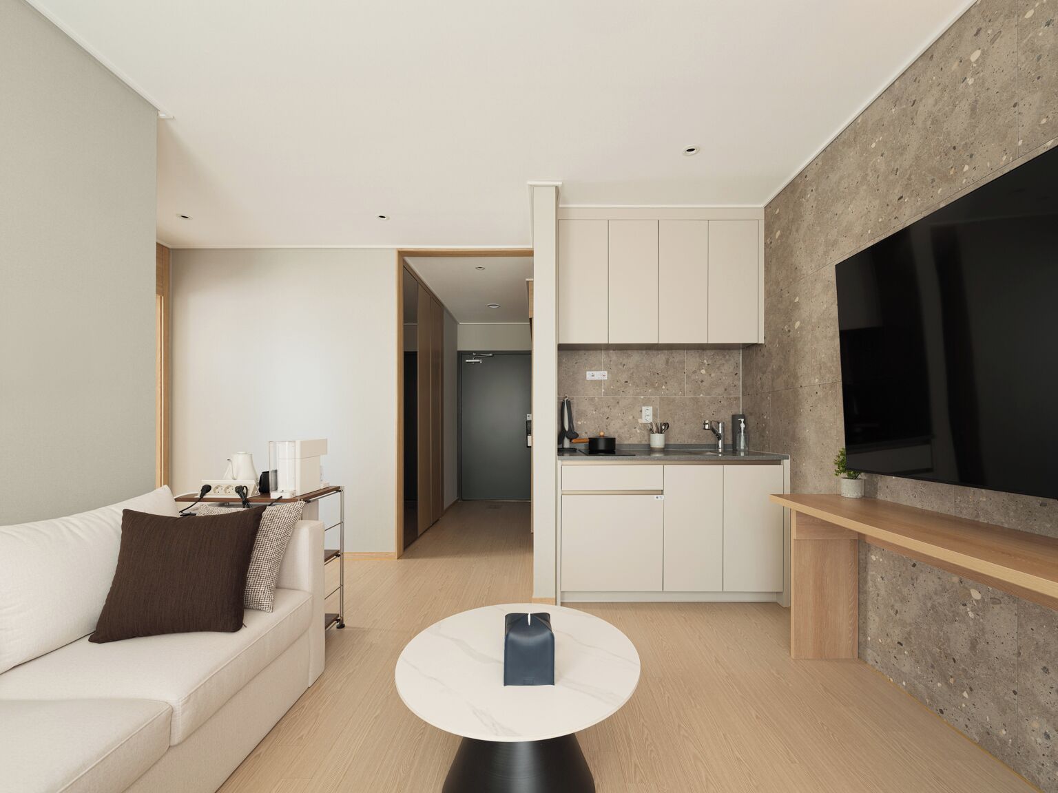 A modern living room with a sofa, a coffee table, and a kitchen area with cabinets and a large TV.