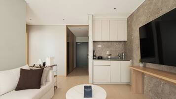 A modern living room with a sofa, a coffee table, and a kitchen area with cabinets and a large TV.