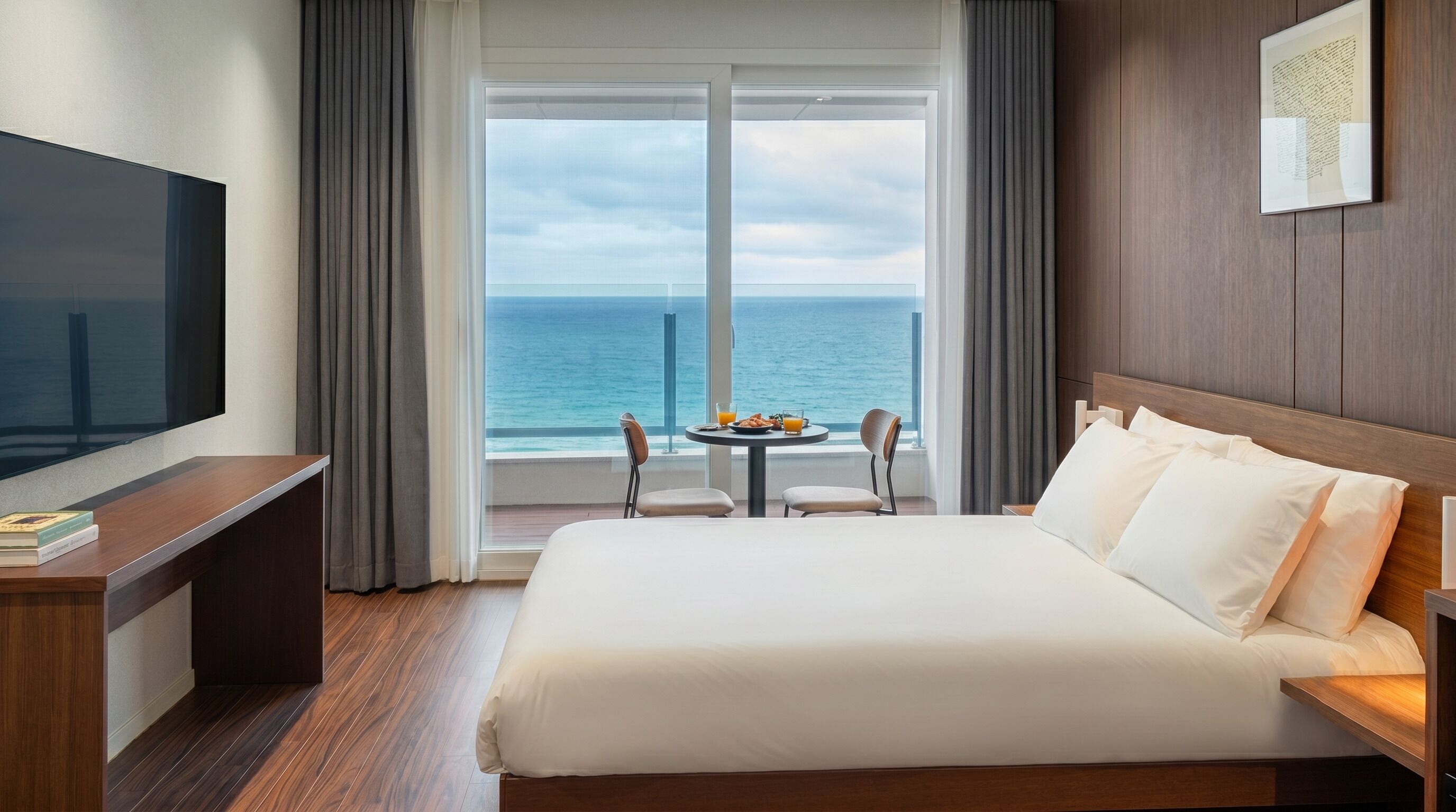 Ein Hotelzimmer mit Bett, Fernseher, Esstisch und Stühlen sowie Blick auf den Ozean.