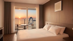 Habitación de hotel con una cama grande, una mesita, dos sillas, vistas al atardecer y una noria.