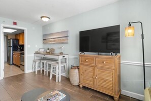 A modern living room with a flat-screen TV, wooden cabinet, and a dining area with stools. - Beachside Bliss: Oceanfront Suite w/ Breakfast (Myrtle Beach)