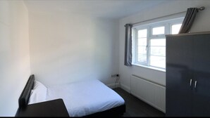 Et lille, enkelt værelse med seng, garderobe og et vindue med gardiner.